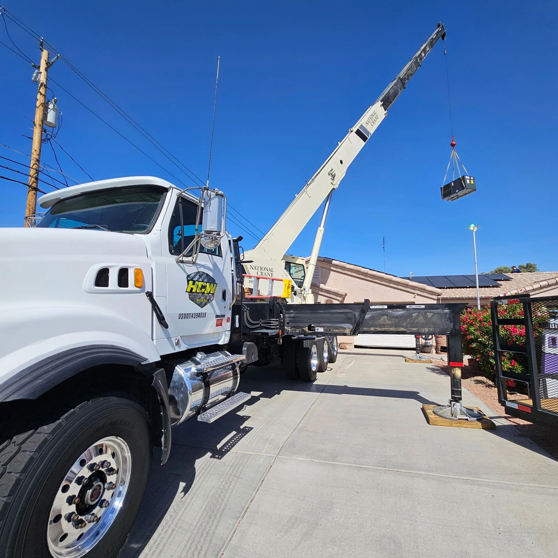 Boom truck crane lifting a rooftop HVAC unit over a home driveway on a clear day